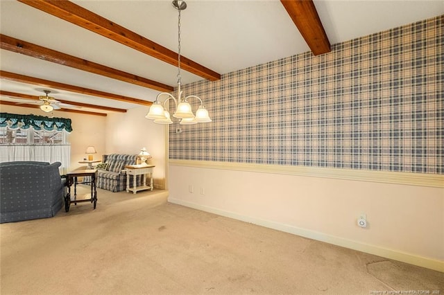 carpeted living area with ceiling fan with notable chandelier, a wainscoted wall, baseboards, beamed ceiling, and wallpapered walls