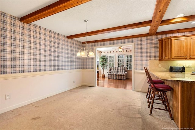 dining room with a wainscoted wall, beamed ceiling, light carpet, and wallpapered walls