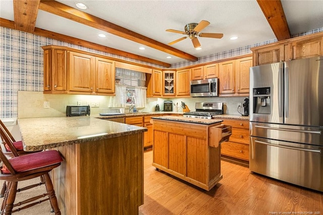 kitchen featuring wallpapered walls, a peninsula, stainless steel appliances, light wood-type flooring, and beam ceiling