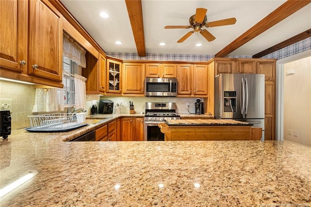 kitchen featuring beam ceiling, brown cabinets, appliances with stainless steel finishes, glass insert cabinets, and light stone countertops