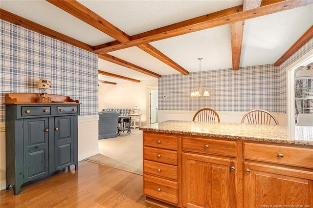 kitchen featuring light stone countertops, wallpapered walls, light wood-style floors, and beamed ceiling