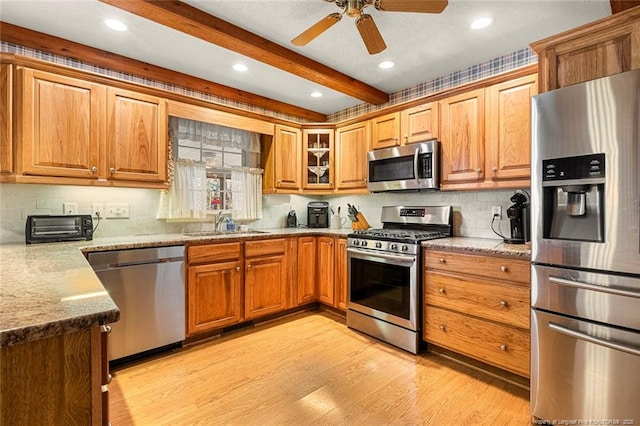 kitchen featuring brown cabinetry, light wood-style flooring, appliances with stainless steel finishes, beamed ceiling, and a sink