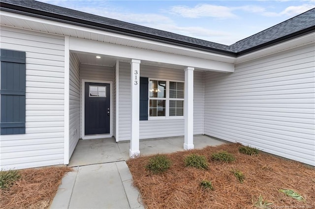 entrance to property with a porch and roof with shingles