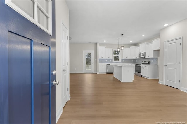 kitchen with appliances with stainless steel finishes, a center island, light wood-style floors, white cabinetry, and backsplash