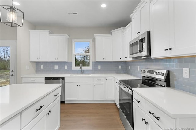 kitchen featuring light wood-style flooring, a sink, white cabinetry, light countertops, and appliances with stainless steel finishes