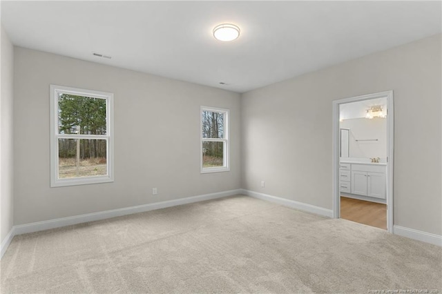 unfurnished bedroom with light carpet, baseboards, visible vents, and ensuite bathroom