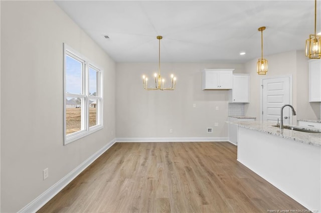 unfurnished dining area with light wood finished floors, visible vents, baseboards, an inviting chandelier, and a sink