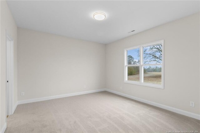 spare room featuring light carpet and baseboards