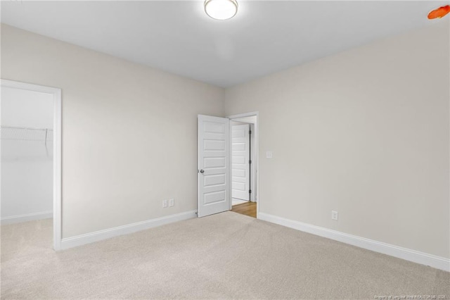 unfurnished bedroom with a closet, carpet, a walk in closet, and baseboards