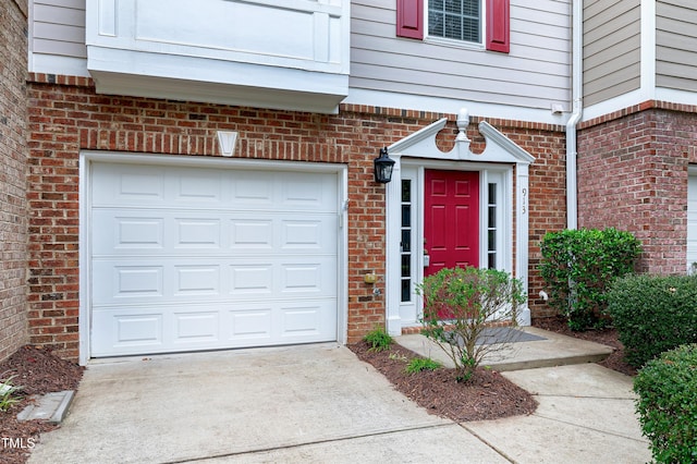 entrance to property featuring a garage, concrete driveway, and brick siding