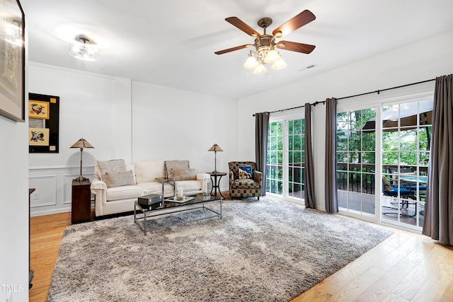 living room with visible vents, a decorative wall, wainscoting, ceiling fan, and wood finished floors