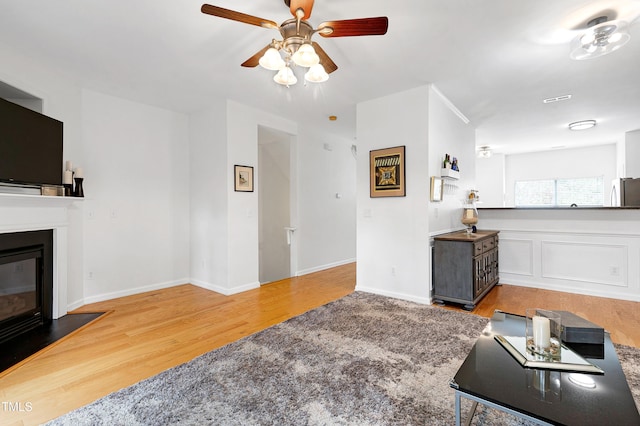 living room featuring a ceiling fan, a glass covered fireplace, baseboards, and wood finished floors