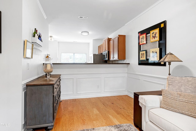 kitchen with dark countertops, ornamental molding, brown cabinets, stainless steel appliances, and light wood-style floors