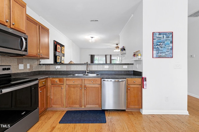 kitchen featuring a sink, appliances with stainless steel finishes, light wood-type flooring, brown cabinetry, and dark countertops