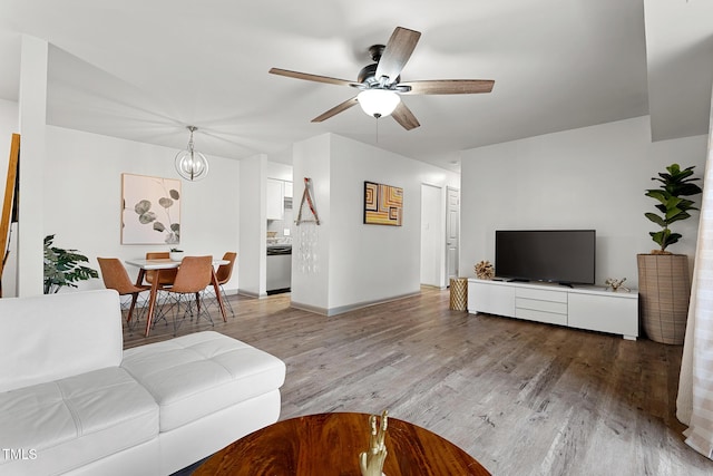 living area with ceiling fan with notable chandelier, light wood-style floors, and baseboards