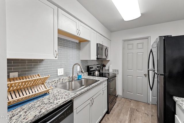 kitchen with decorative backsplash, light wood-style floors, white cabinets, black appliances, and a sink