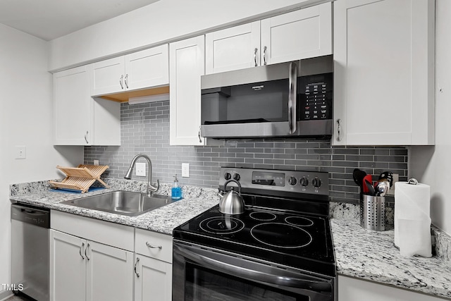 kitchen with light stone counters, a sink, decorative backsplash, white cabinets, and appliances with stainless steel finishes