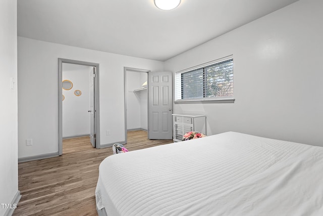 bedroom featuring baseboards, wood finished floors, and a spacious closet