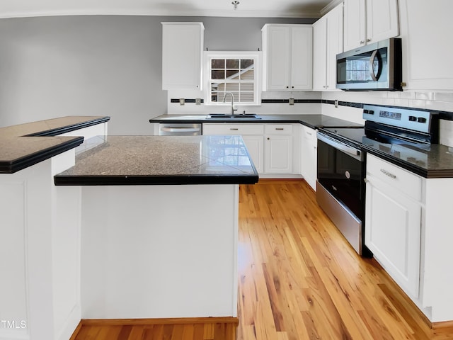 kitchen featuring stainless steel appliances, light wood finished floors, a sink, and white cabinetry