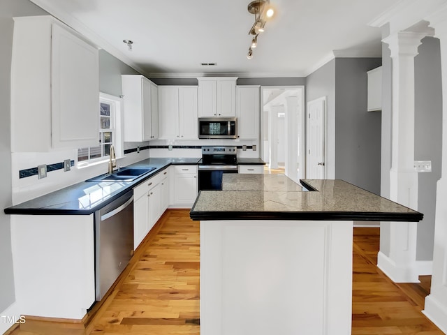 kitchen with stainless steel appliances, a kitchen island, a sink, white cabinetry, and ornamental molding