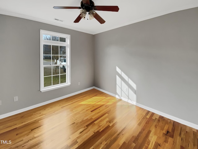 empty room with crown molding, visible vents, ceiling fan, wood finished floors, and baseboards