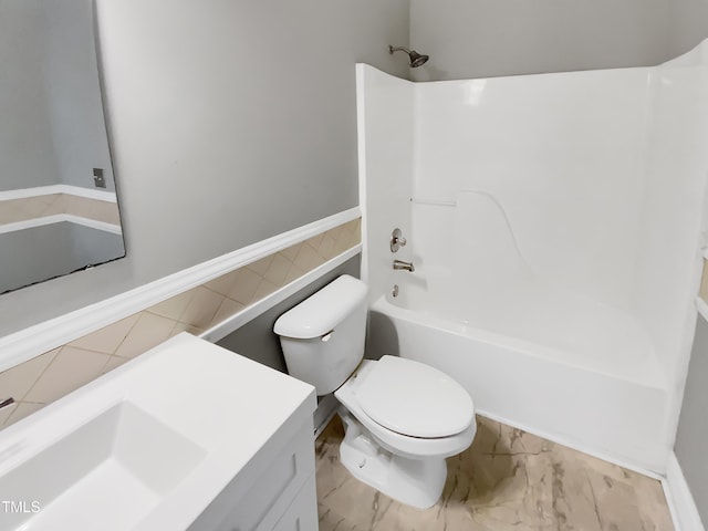 full bathroom with marble finish floor, toilet, washtub / shower combination, wainscoting, and vanity