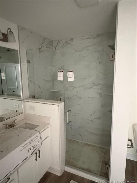bathroom featuring a marble finish shower, wood finished floors, and vanity