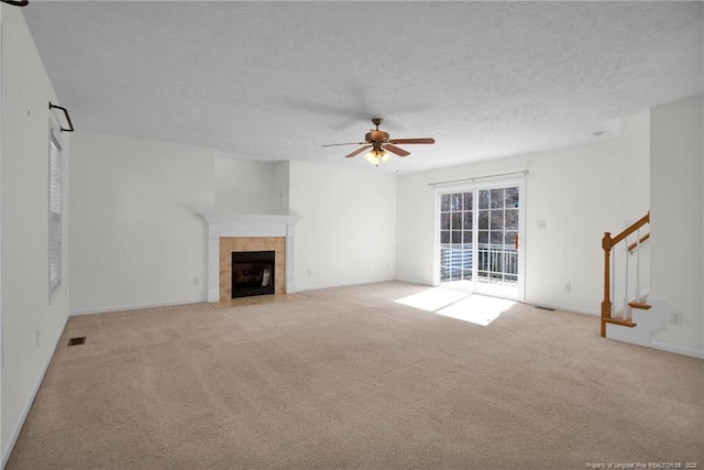 unfurnished living room featuring visible vents, light colored carpet, stairway, a textured ceiling, and a tile fireplace