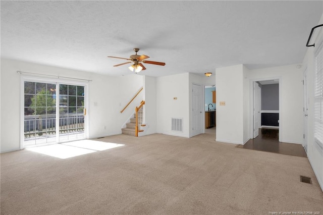 unfurnished living room with visible vents, stairway, and carpet flooring