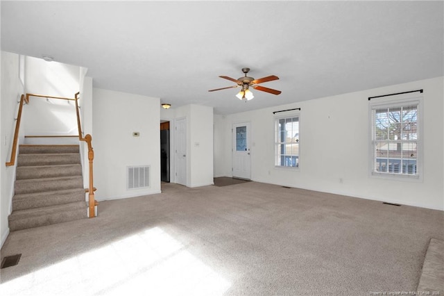 unfurnished living room with carpet, visible vents, ceiling fan, and stairs