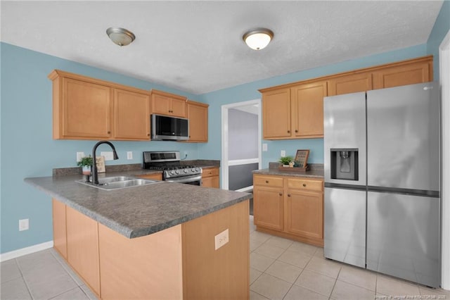 kitchen featuring light tile patterned floors, dark countertops, a peninsula, stainless steel appliances, and a sink