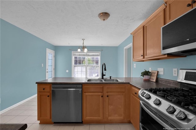 kitchen with dark countertops, appliances with stainless steel finishes, a sink, a textured ceiling, and a peninsula