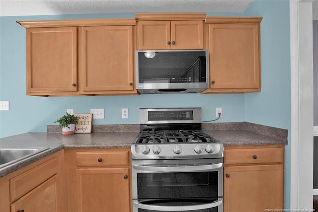 kitchen featuring dark countertops, appliances with stainless steel finishes, and light brown cabinetry