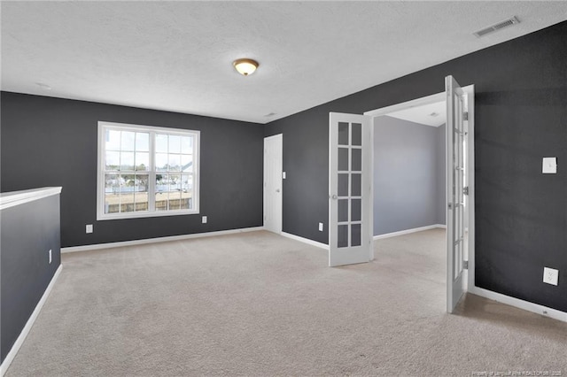 carpeted spare room featuring baseboards, visible vents, a textured ceiling, and french doors