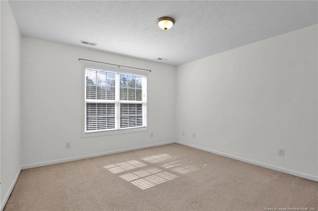 carpeted spare room featuring visible vents, a textured ceiling, and baseboards