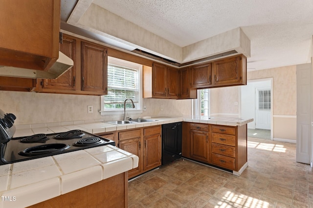 kitchen featuring tile counters, a sink, a peninsula, under cabinet range hood, and black appliances