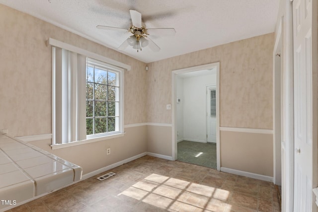 spare room with a textured ceiling, baseboards, visible vents, and a ceiling fan