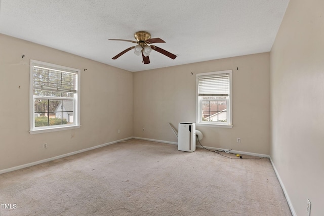 carpeted empty room with a healthy amount of sunlight, a ceiling fan, baseboards, and a textured ceiling