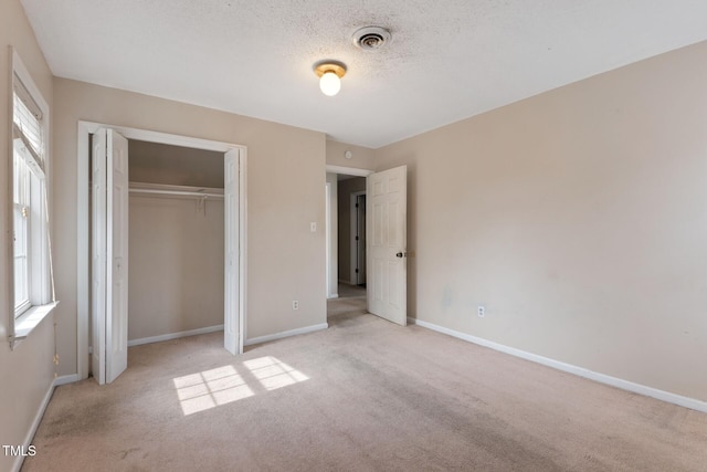 unfurnished bedroom featuring visible vents, baseboards, light colored carpet, a textured ceiling, and a closet