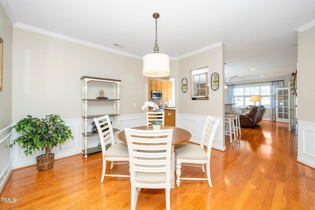 dining space featuring a wainscoted wall, light wood finished floors, visible vents, and crown molding