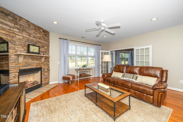 living room featuring baseboards, visible vents, wood finished floors, a stone fireplace, and recessed lighting