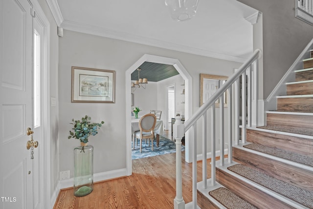 foyer entrance featuring stairway, wood finished floors, baseboards, an inviting chandelier, and crown molding