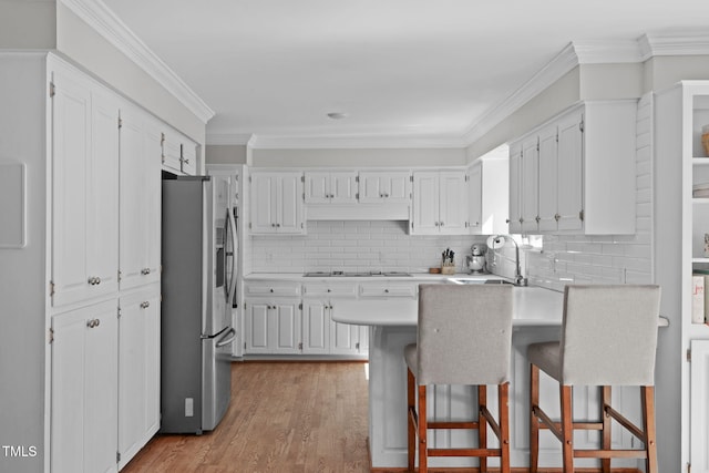 kitchen featuring white stovetop, a peninsula, freestanding refrigerator, white cabinets, and a sink