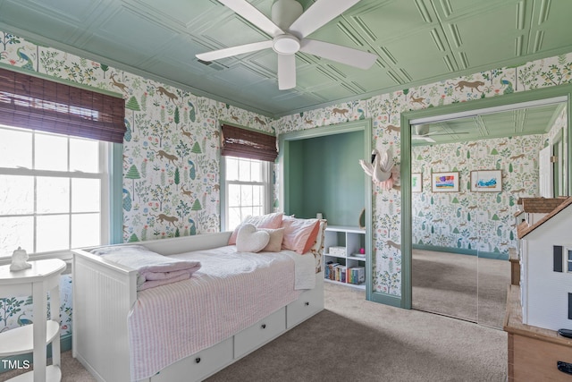 carpeted bedroom featuring wallpapered walls, a ceiling fan, and an ornate ceiling