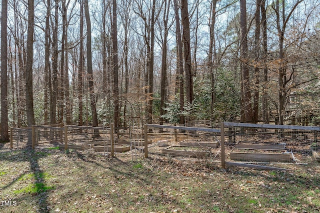 view of yard with a vegetable garden, fence, and a wooded view