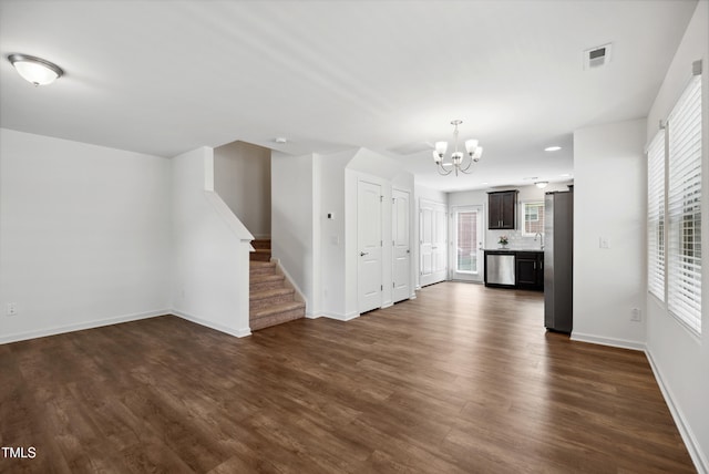 unfurnished living room with a chandelier, dark wood-style floors, stairway, baseboards, and plenty of natural light