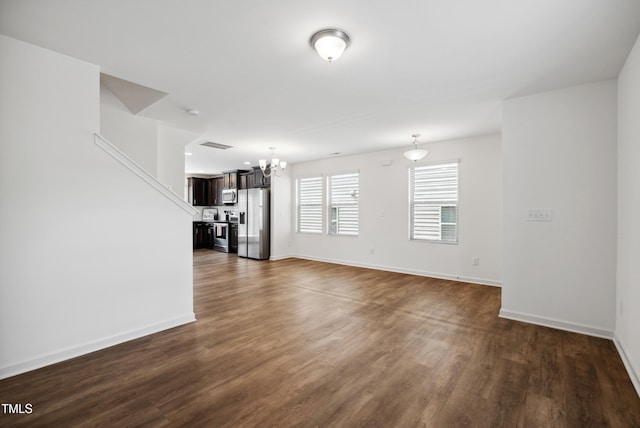 unfurnished living room featuring a chandelier, dark wood finished floors, and baseboards