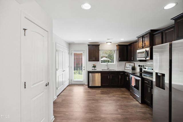 kitchen featuring stainless steel appliances, a sink, decorative backsplash, dark wood-type flooring, and dark brown cabinets