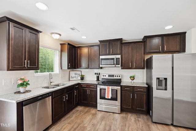 kitchen featuring stainless steel appliances, a sink, dark brown cabinets, and light wood finished floors
