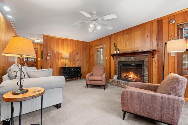 living area with light colored carpet, wooden walls, a brick fireplace, and a ceiling fan